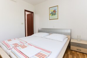 A neatly made bed with striped bedding, a bedside table with a glass container, and a painting on the wall. - Apartment in Dubrovnik with swimming pool and sea view   (A2) (Dubrovnik Mokosica)