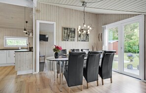 A modern kitchen with wooden paneling, a dining area with black leather chairs, and a large sliding glass door leading to a garden. - Nice home in Oksbøl with WiFi (Oksbøl)