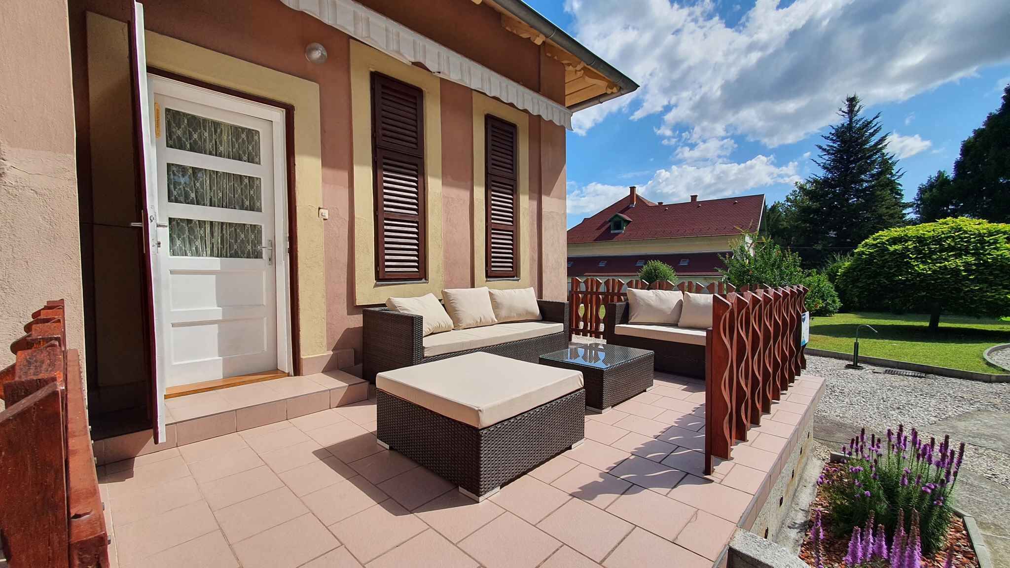 A covered outdoor seating area with wicker furniture and a door leading to a building.