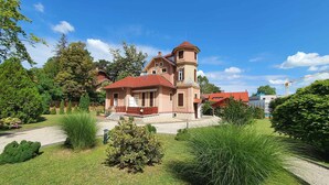 Ein zweistöckiges Haus mit rotem Dach, einem turmartigen Aufbau und einem gepflegten Garten.