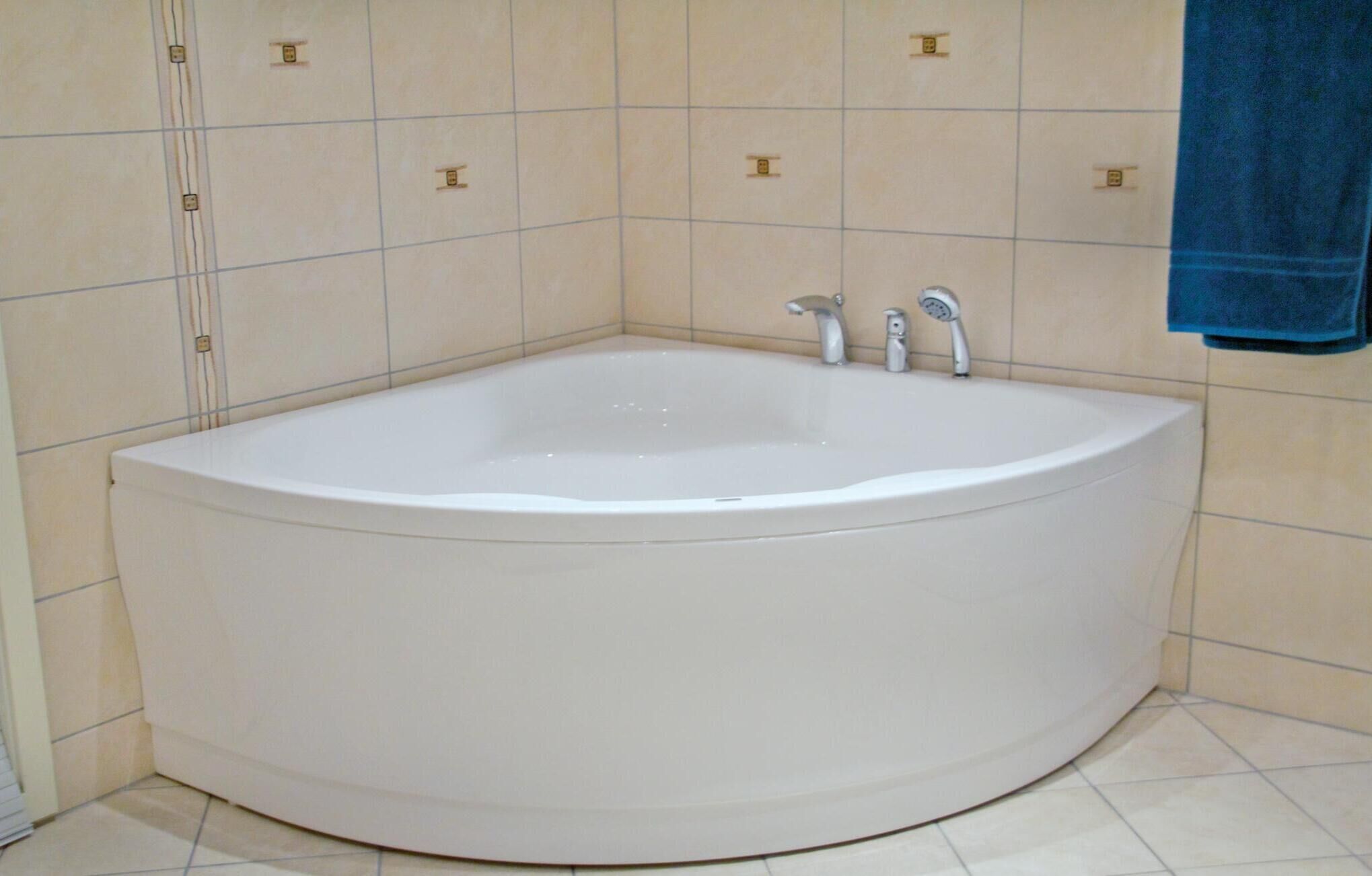 Una vasca da bagno freestanding ampia e bianca in un bagno con piastrelle color beige e un asciugamano blu appeso al muro.