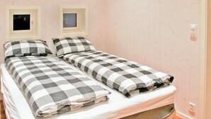 Ein Doppelbett mit kariertem Überwurf in einem Zimmer mit Holzwänden und zwei kleinen Bilderrahmen an der Wand.