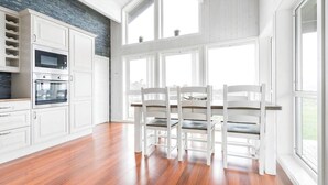 Eine moderne Küche mit weißen Schränken, einem eingebauten Backofen und einem Essbereich mit weißen Stühlen und einem Holztisch.