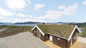 Eine zweistöckige Holzhütte mit einer Holzterrasse und Blick auf einen See und Berge.