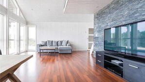 Ein modernes Wohnzimmer mit einem grauen Sofa, einem Holztisch und einem großen Flachbildfernseher, der an einer strukturierten Wand angebracht ist.