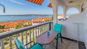 Een balkon met een tafel en stoelen, uitkijkend op een kustplaatsje met rode daken en uitzicht op zee.