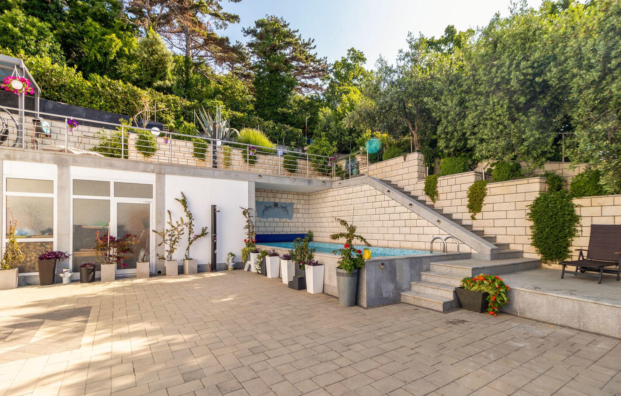 Ein moderner Außenbereich mit Terrasse, Pool, Steinpodesten und Topfpflanzen.