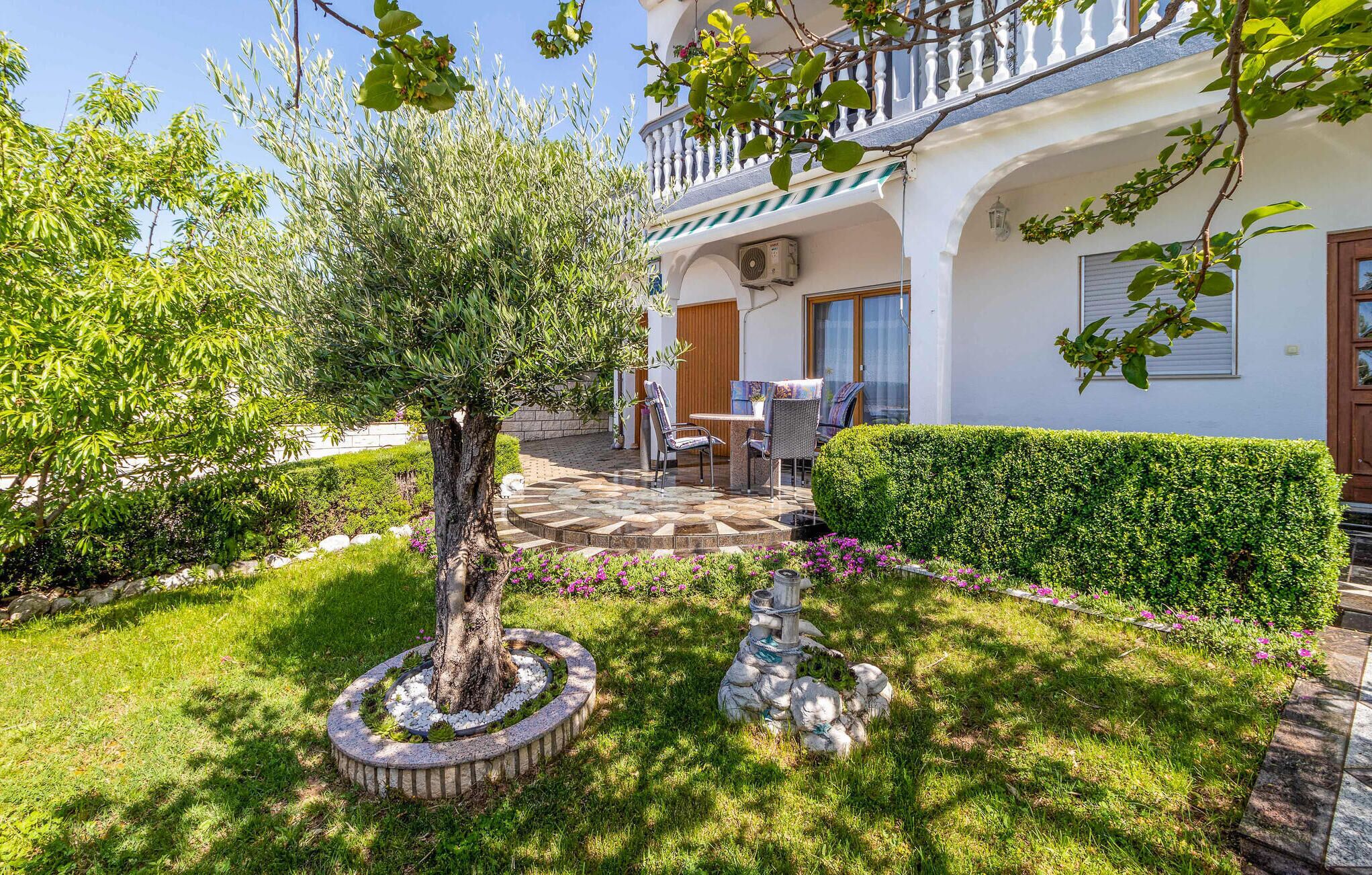 Un jardín bien cuidado con un árbol central, un banco de piedra y un patio amoblado.