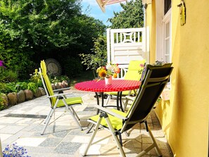 Een terras buiten met een ronde tafel, gele stoelen en een gele muur.