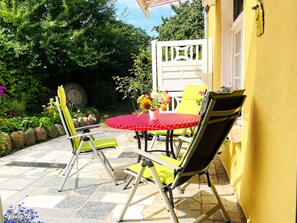 An outdoor patio with a round table, yellow chairs, and a yellow wall.