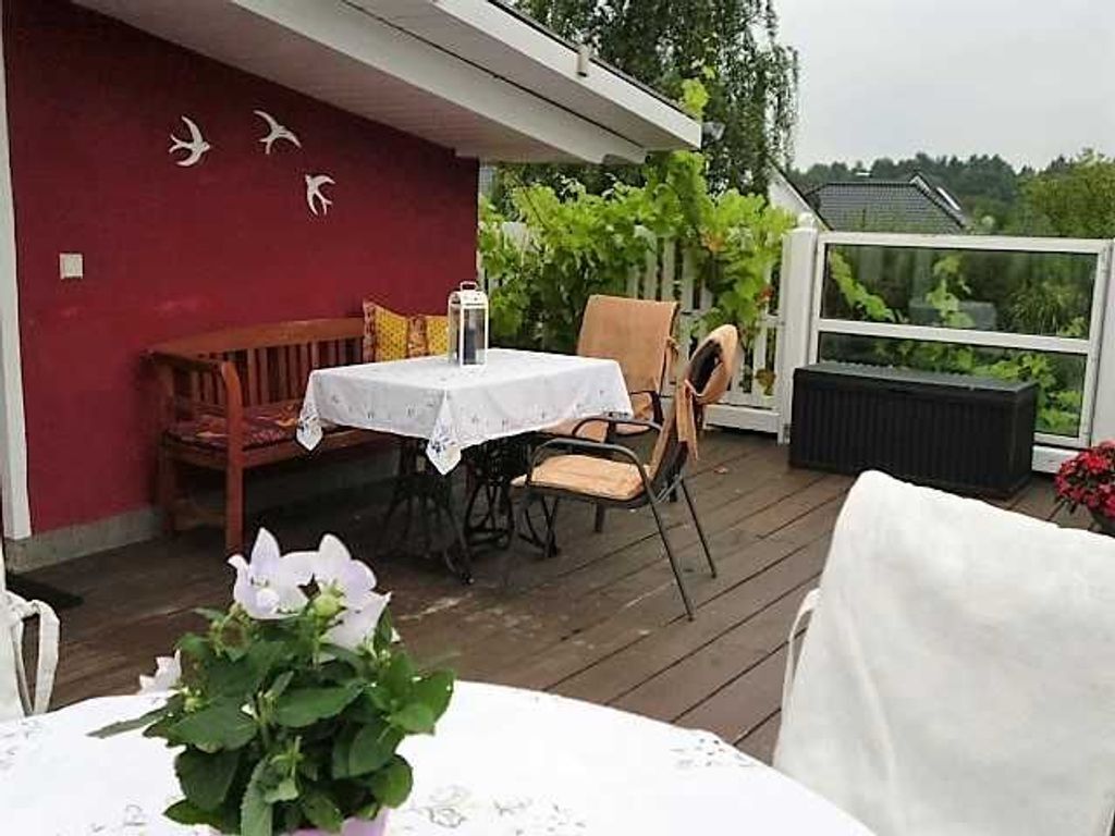 Ein überdachter Außenbereich zum Essen mit Tisch, Stühlen, einer Bank und einem Topfpflanzen.