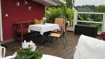 Ein überdachter Außenbereich zum Essen mit Tisch, Stühlen, einer Bank und einem Topfpflanzen.