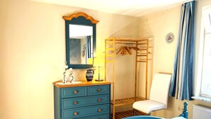 A bedroom with a bed, dresser, mirror, and a wooden wardrobe with hanging space. - Apartment Schwalbennest - House Gundelrebe (Bergen auf Rügen)