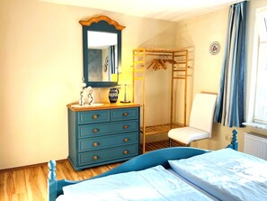 A bedroom with a bed, dresser, mirror, and a wooden wardrobe with hanging space.