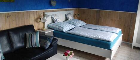 A bedroom with a bed, a black leather sofa, a white table, and a small vase with flowers.