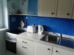 Una cocina con estufa, tostadora, tetera, lavabo y armarios.