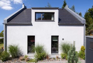 A modern two-story house with a sloped roof, large windows, and a small balcony.