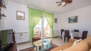 Un salon comprenant une table basse en verre, un canapé, un téléviseur et un coin repas avec des chaises et une table.