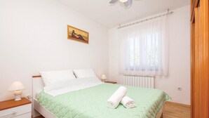 Un lit bien fait, avec une couette verte, des oreillers blancs et des serviettes enroulées, posé sur un plancher en bois.