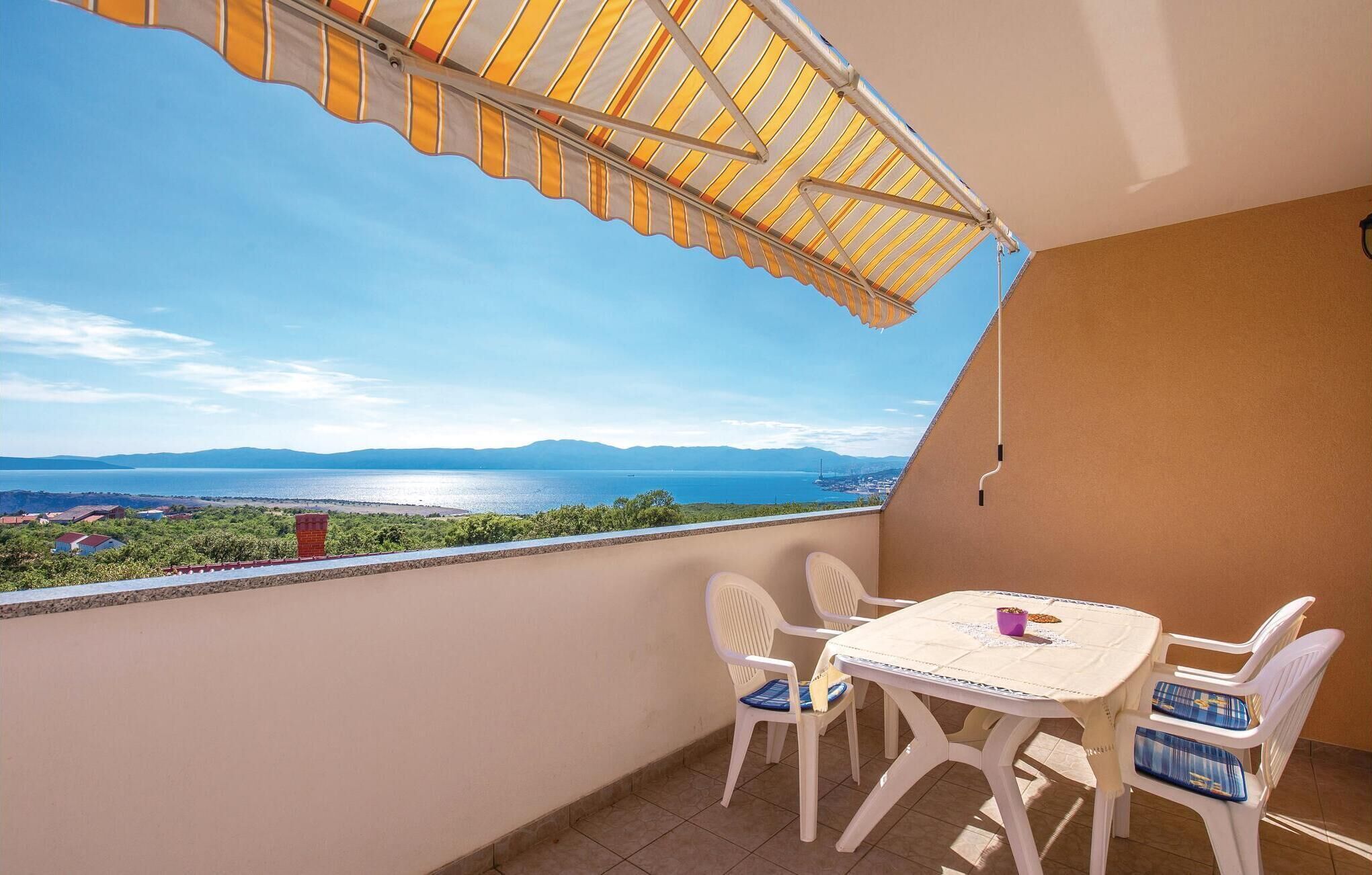 Un balcon avec une table et des chaises, offrant une vue panoramique sur une étendue d’eau et des montagnes lointaines.