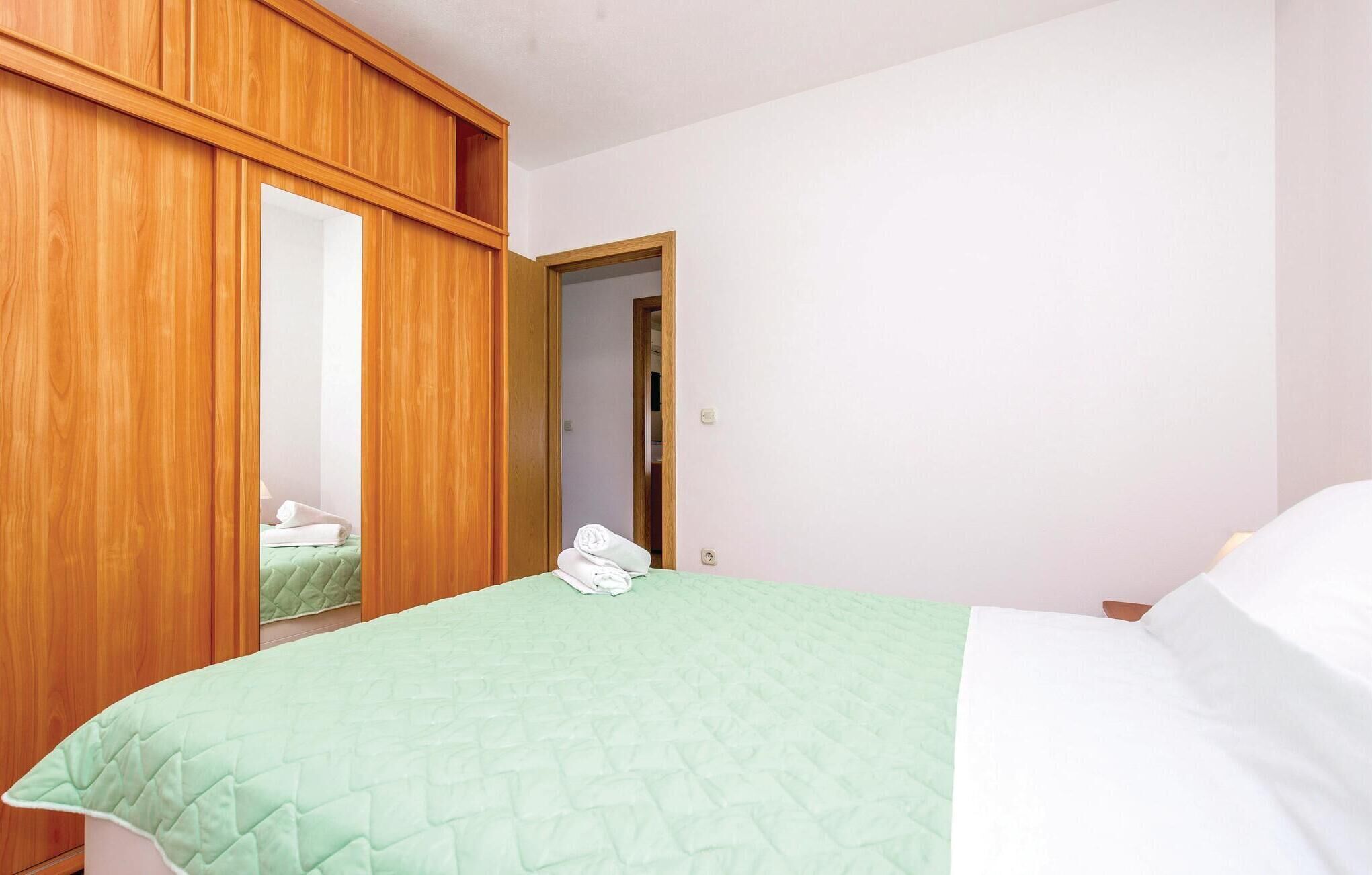 A bedroom with a bed, a wooden wardrobe, and a mirror.
