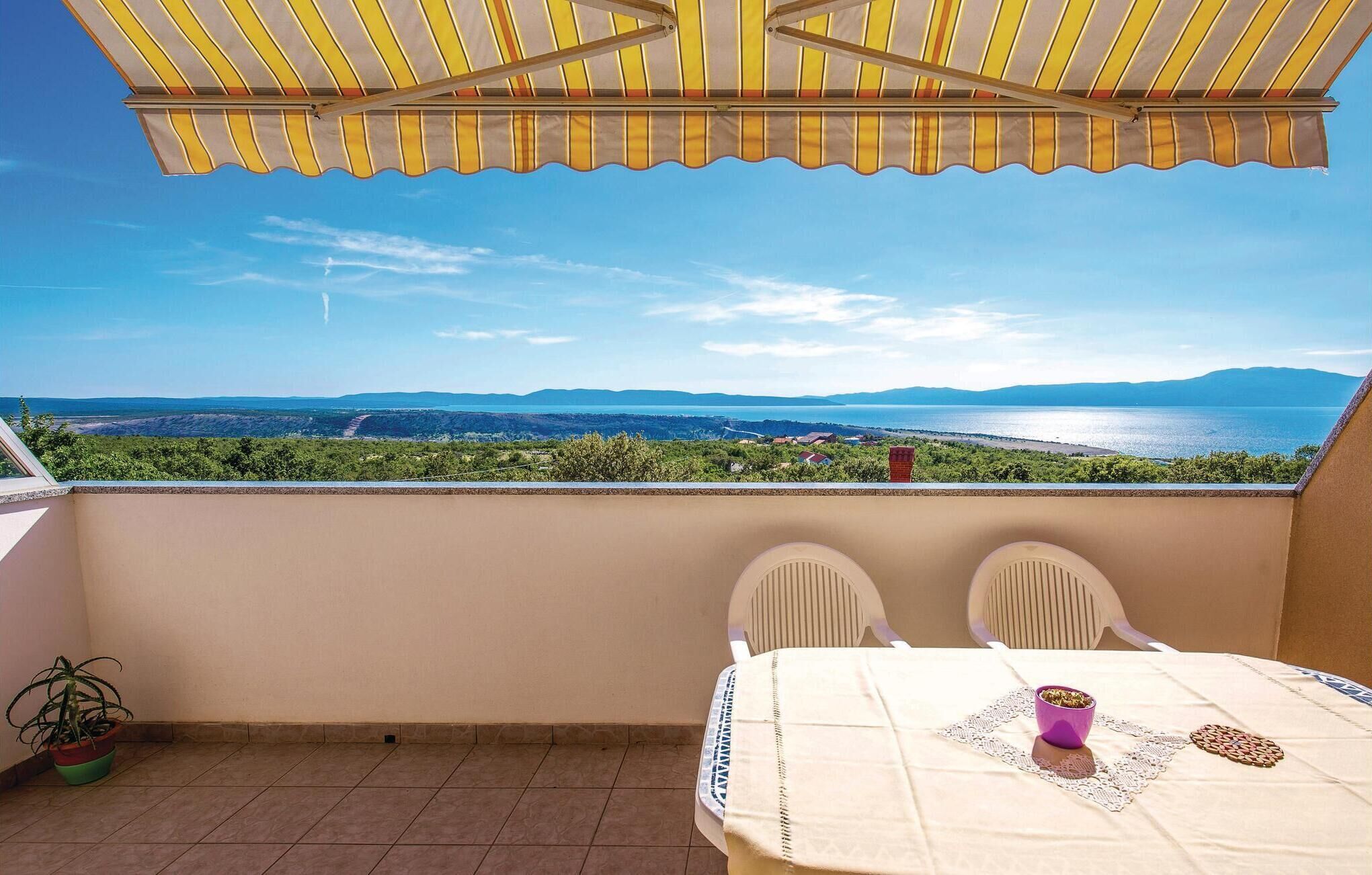 Un balcón con vistas a un paisaje costero, una mesa con sillas y una planta en maceta.