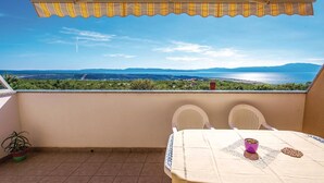 Un balcon donnant sur un paysage côtier, une table avec des chaises et une plante en pot.