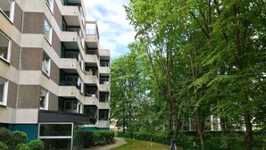 A multi-story residential building with balconies, a grassy courtyard, and surrounding trees.