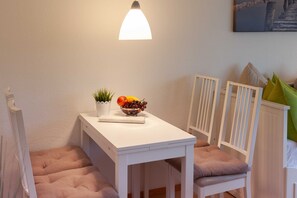A white table with a bowl of fruit and a small plant, a white chair with a cushion, and a white radiator.