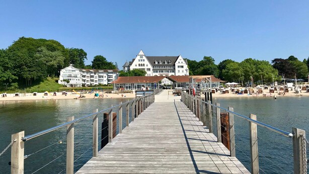 A wooden pier leading to a beach with a large white building in the background.