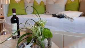 A neatly arranged room with a bed, pillows, a wine bottle, and a vase with flowers.