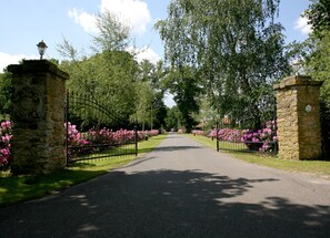 A paved pathway flanked by stone pillars and metal gates, leading through a garden with pink flowers.