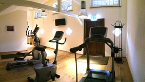 Ein Fitnessraum mit Trainingsgeräten, Holzboden und einer Tür im Hintergrund.