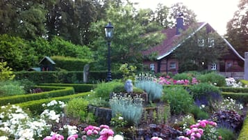 A garden with a variety of flowers, a stone sculpture, and a traditional house in the background.