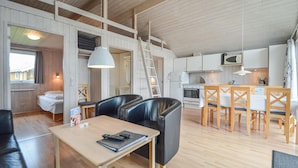 Un espacio habitable moderno y abierto con piso de madera, un comedor con sillas de madera, una cocina con gabinetes blancos y un altillo con escalera.