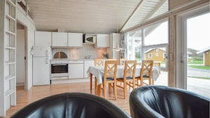 Cocina compacta con armarios blancos, microondas y estufa. Hay una mesa de comedor con sillas y vistas a un edificio amarillo en el exterior.