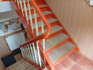 A staircase with white balusters and orange handrails, leading to a landing with a bulletin board and a radiator.