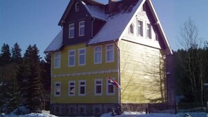 A two-story building with a gabled roof, multiple windows, and a flagpole.