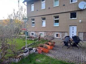 A residential building with a brick exterior, a satellite dish, and a small garden area with potted plants and outdoor furniture.