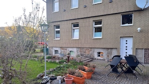 A residential building with a brick exterior, a satellite dish, and a small garden area with potted plants and outdoor furniture.