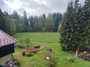 A residential property with a brick house, a green lawn, a wooden deck, and a dense forest in the background.