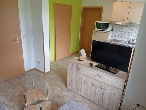 A compact kitchen with a microwave, a television, and a small cabinet.