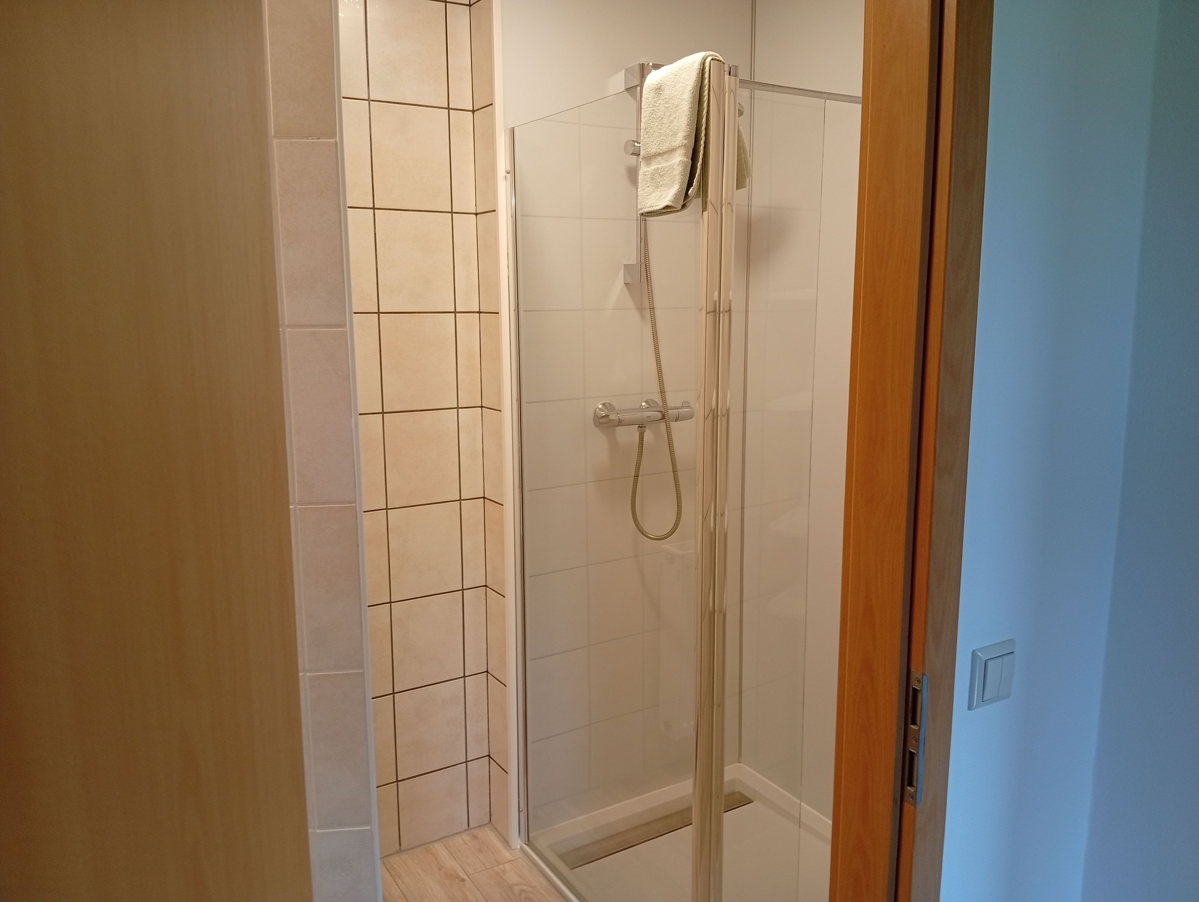 A glass-enclosed shower with a handheld showerhead and a towel hanging on the wall.