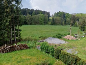 Paisagem rural com um grande campo aberto, uma pilha de lenha e uma pequena pilha de fogueira.
