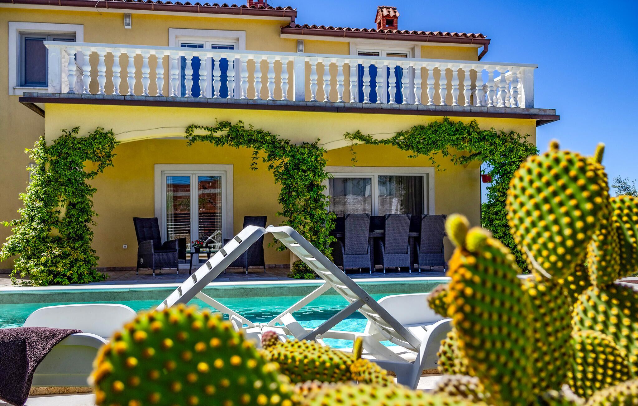 A two-story house with a swimming pool, outdoor seating, and cacti.