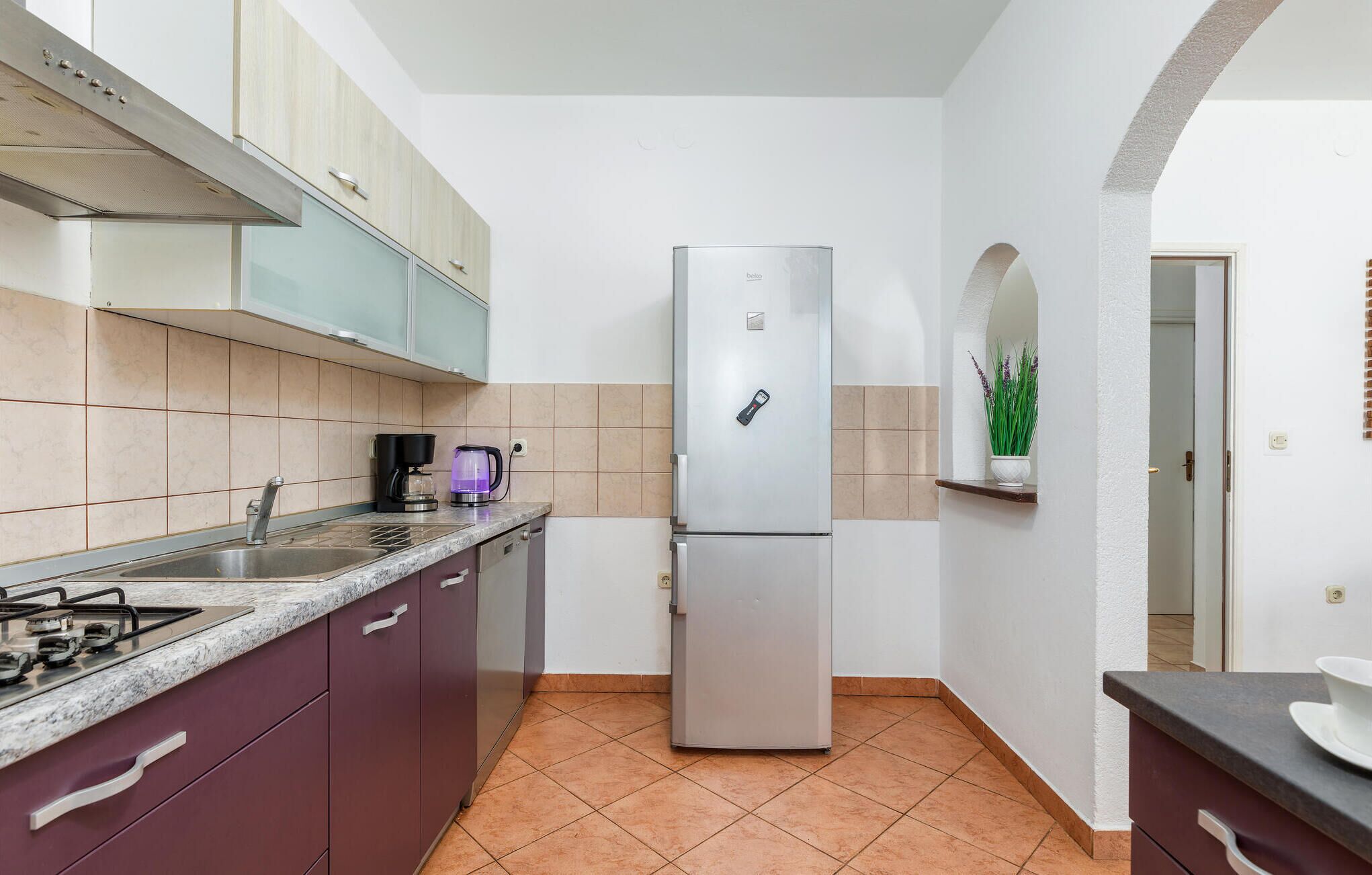 Una cocina compacta con un refrigerador de acero inoxidable, una estufa a gas, una cafetera y un lavamanos.
