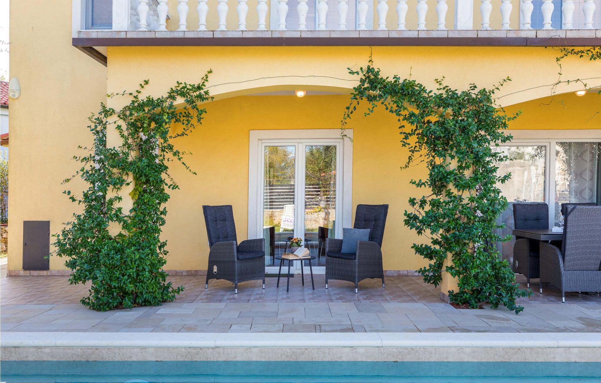 An outdoor seating area with wicker furniture, a pool, and a yellow building facade.