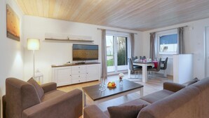 Ein modernes Wohnzimmer mit Flachbildfernseher, einem Essbereich mit Tisch und Stühlen sowie einer Küchenzeile mit Kühlschrank.