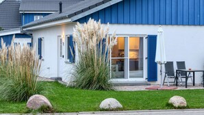 Ein modernes Haus mit blauer Fassade, einer überdachten Terrasse mit Sitzgelegenheit und einem gepflegten Rasen.