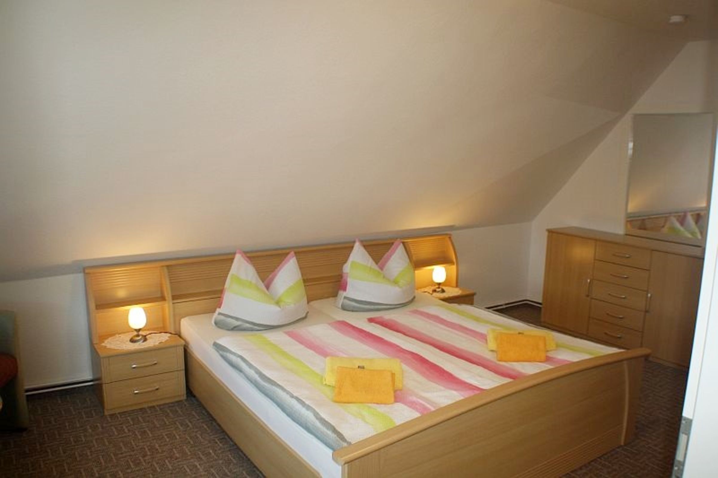 A bedroom with a bed, two bedside tables, a nightstand, a dresser, and a mirror.